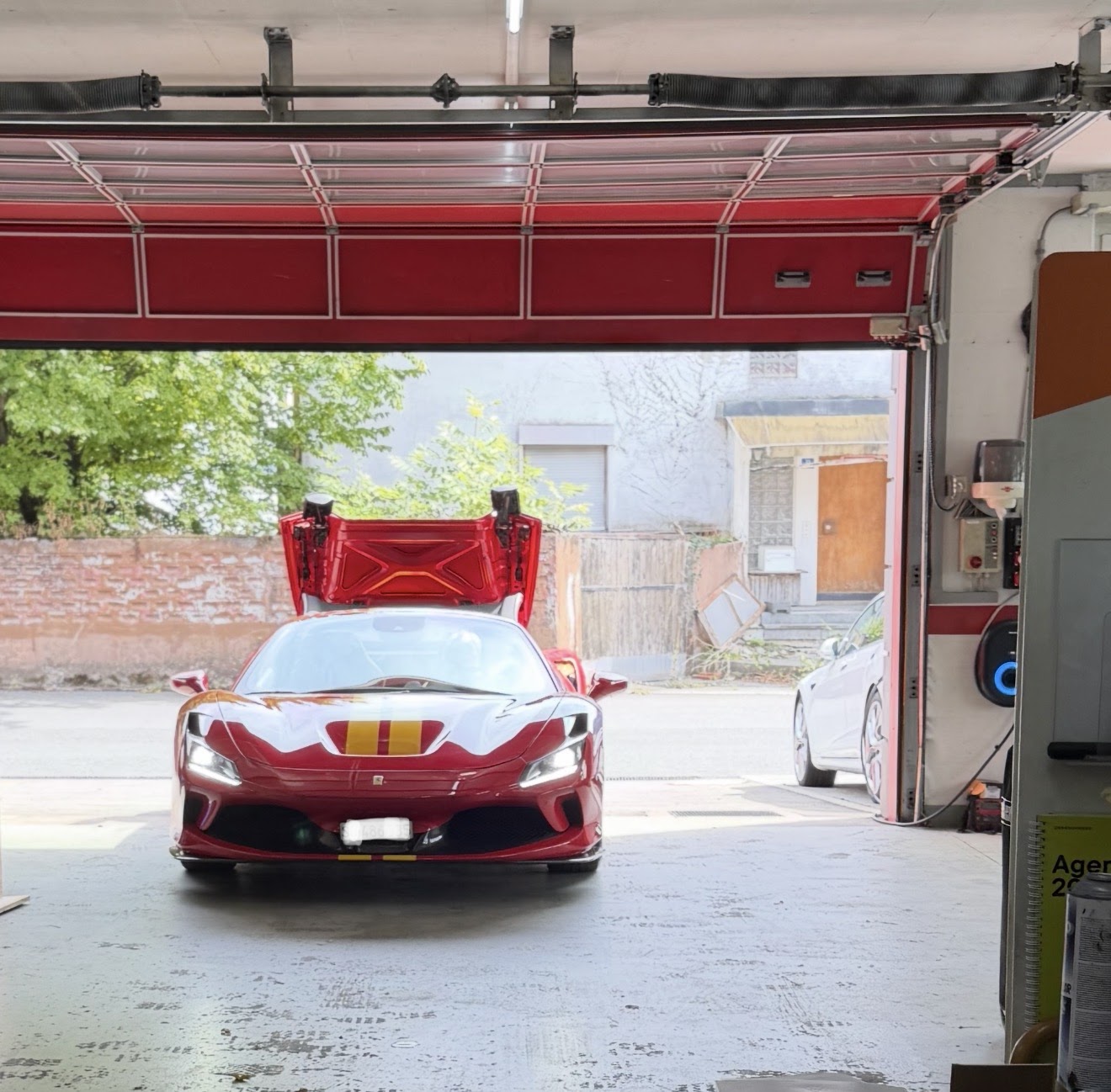 Roter Sportwagen mit geöffneter Motorhaube vor dem Werkstatttor