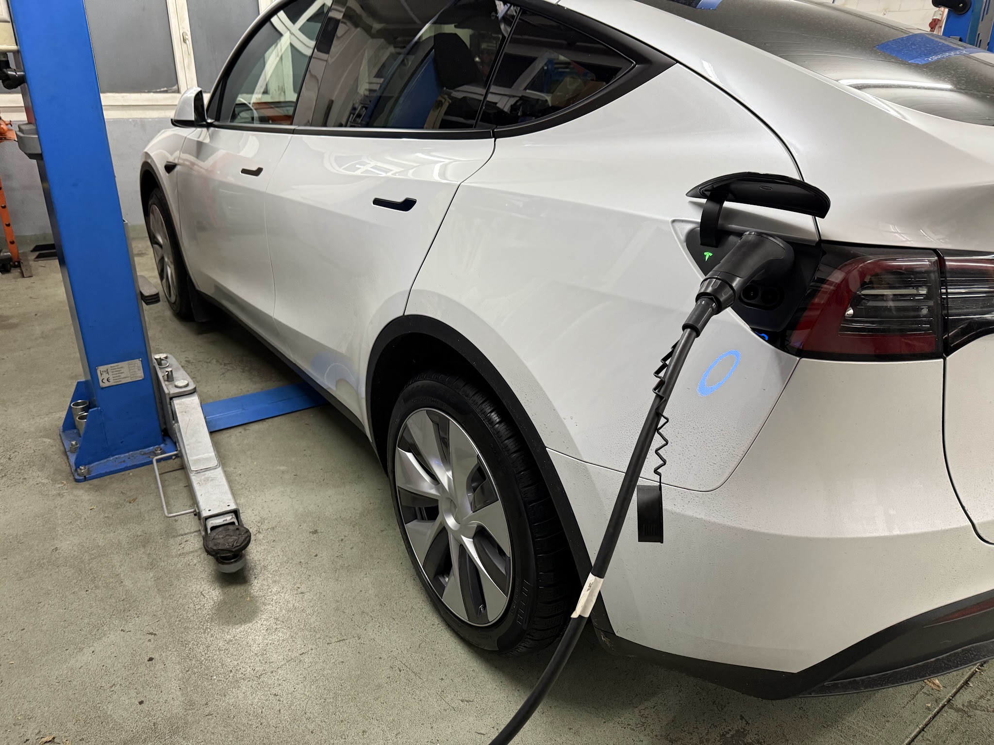 Weisser Tesla Model Y am Ladekabel neben der Hebebühne